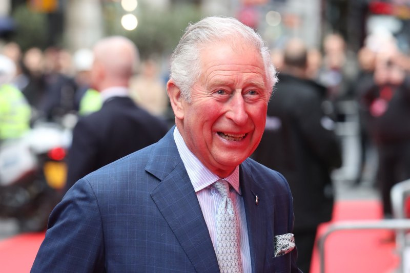   Prins Charles lacht in blauw pak met paarse stropdas