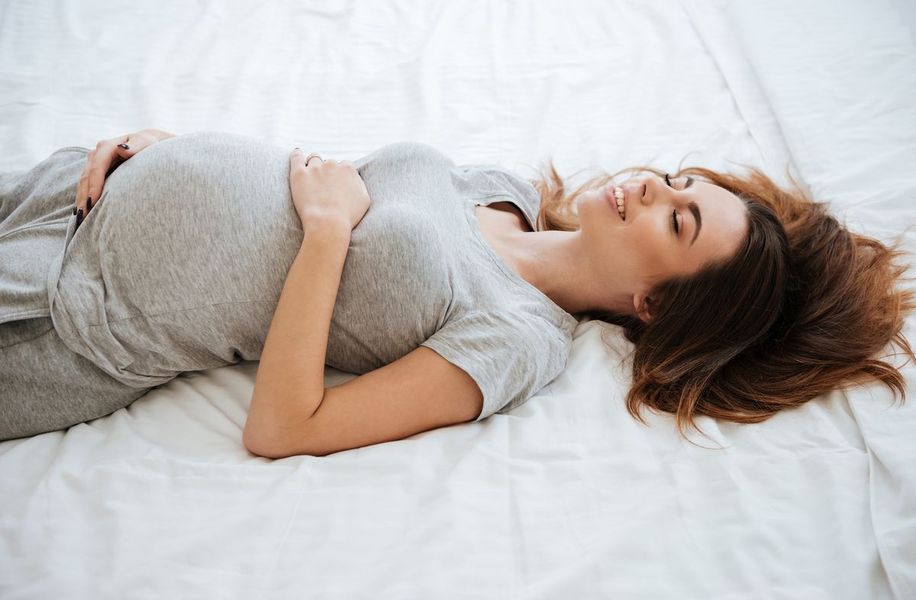 mulher grávida deitada na cama sorrindo